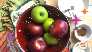 green and red apples in red colander on a printed tea towel with ingredients ready to make apple pie filling