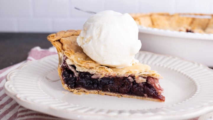 grandma's cherry pie on a white plate with ice cream, and the rest of the pie in a white pie dish in the background
