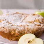 overhead image of french apple cake with slice cut and ready to serve green apples in background
