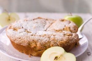 overhead image of french apple cake with slice cut and ready to serve green apples in background