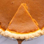 overhead view of pumpkin pie sliced with pie server under a piece of pie