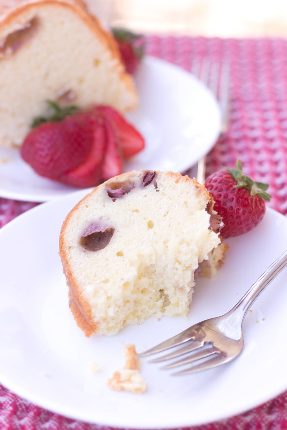 eating a slice of strawberry pound cake with cream cheese fork on white plate and second slice in background
