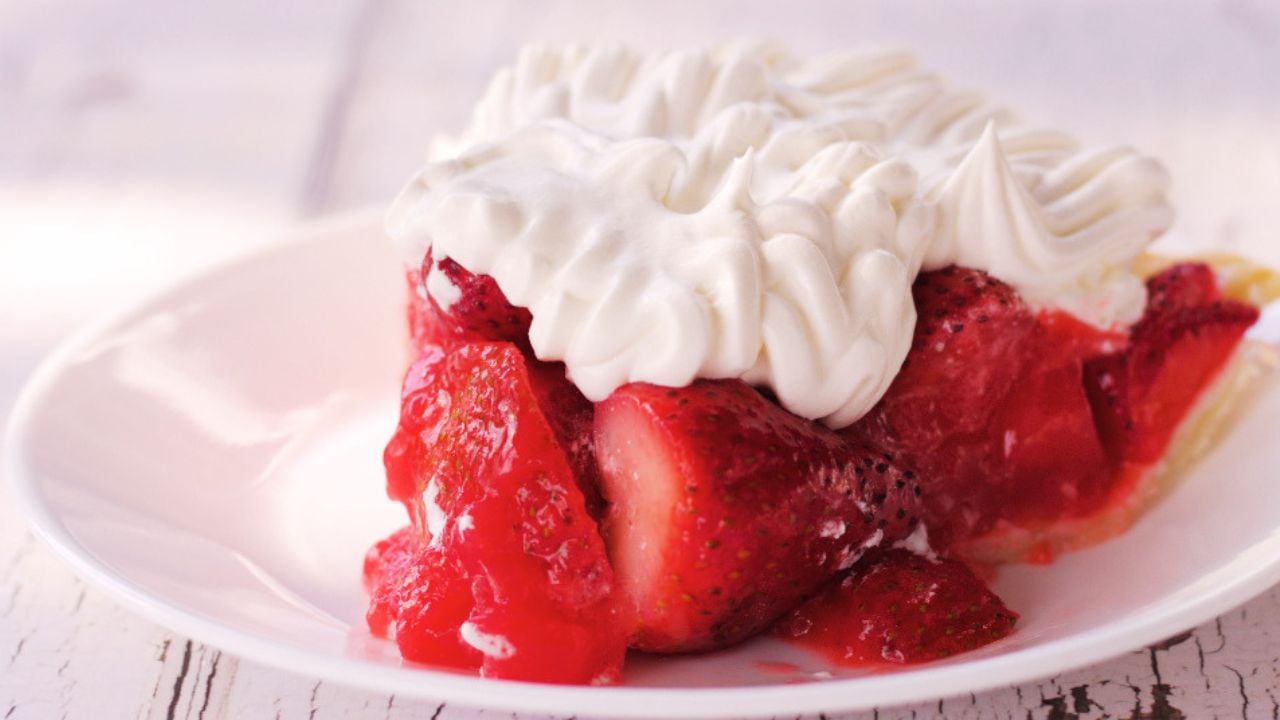 A slice of easy strawberry pie recipe topped with whipped cream is served on a white plate.