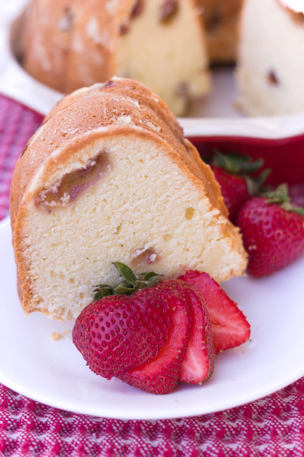 strawberry cream cheese pound cake slice in front of whole cake in red pie plate