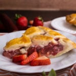 closeup view of strawberry rhubarb pie on white plate with sliced berries