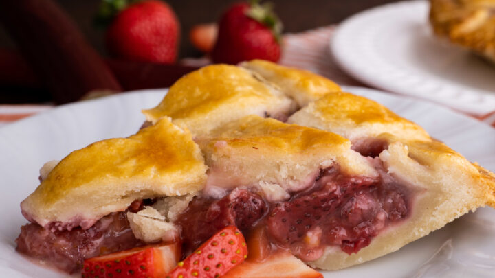closeup view of strawberry rhubarb pie on white plate with sliced berries