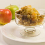 bisquick apple cobbler in footed glass dish on white plate apples in background