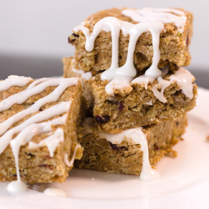 stack of oatmeal squares on white place drizzled with frosting