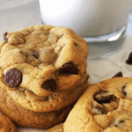 Stack of chocolate chip cookies next to a glass of milk, with scattered chocolate chips on a white surface—these treats look just like they were made from the classic McDonald’s chocolate chip cookie recipe.