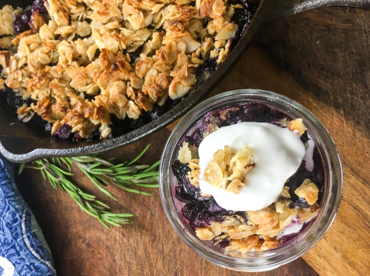 healthy blueberry crisp serving in glass jar with greek yogurt