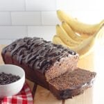 A chocolate banana bread on a cutting board next to a bowl of chocolate chips.