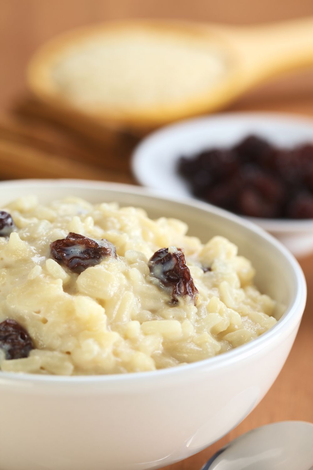 A bowl of rice pudding with raisins, served with a side of bread in the background.