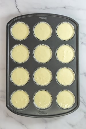A tray of unbaked cupcakes in paper liners, set on a marble countertop.