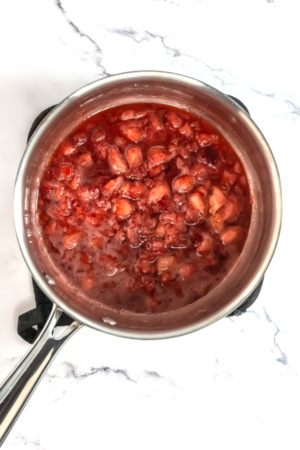Top view of a pot filled with boiling strawberries, cooking on a white marble countertop.
