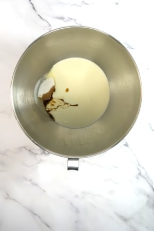 A metal bowl containing milk and a splash of brown syrup on a marble surface.