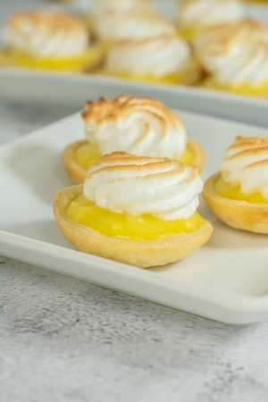 Mini lemon meringue tarts on a white plate, with visible lemon filling and toasted meringue topping.