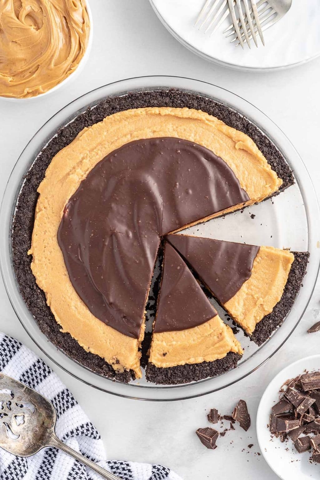 A chocolate and peanut butter pie with an Oreo crust, partially sliced and shown from above on a white surface with plates, forks, and a checked napkin nearby—perfect for easy pie recipes or celebrating National Pie Day.