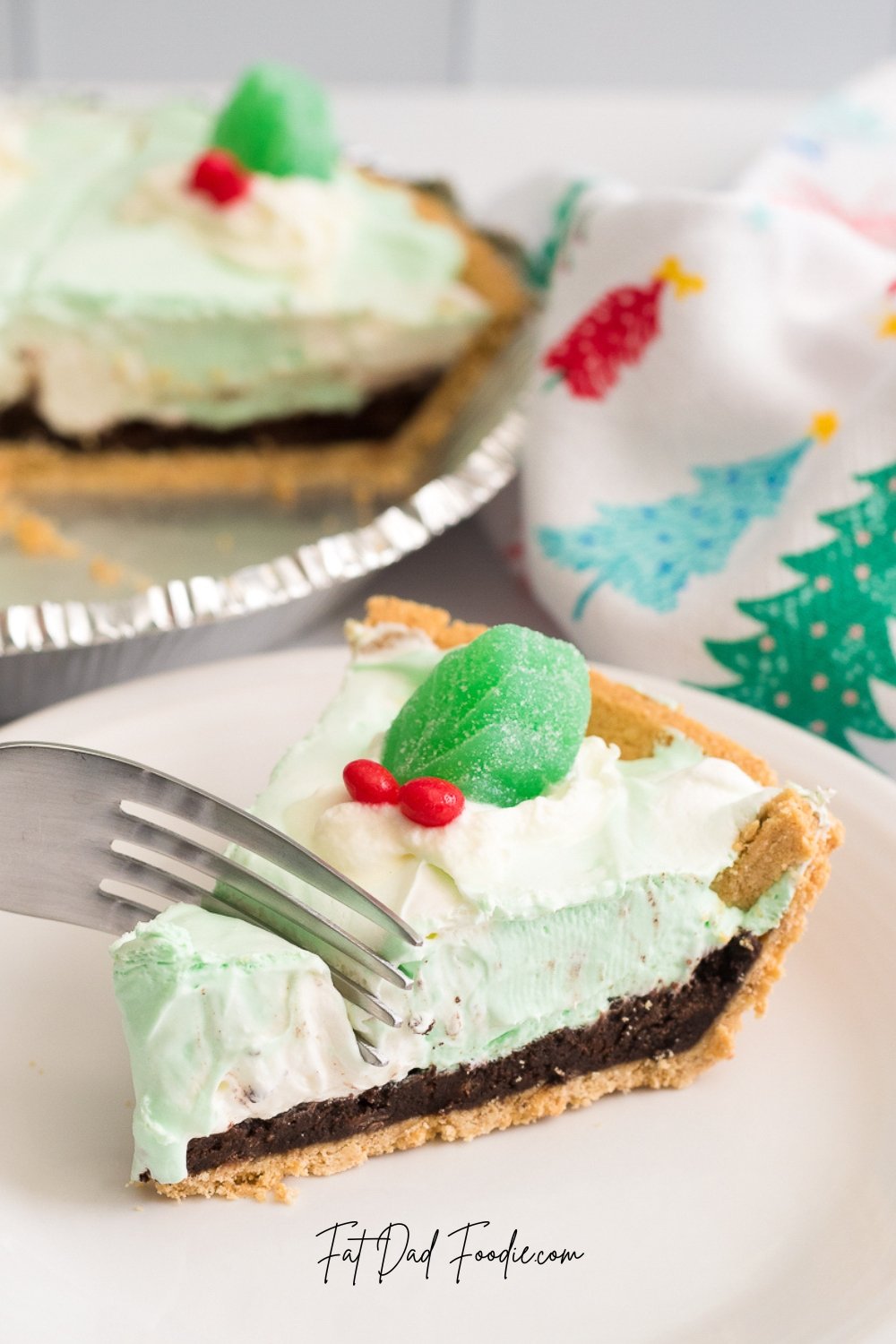 A fork slices into a piece of green mint pie topped with whipped cream, a green candy, and red sprinkles, with the rest of the pie in the background—a festive treat perfect for National Pie Day or your collection of easy pie recipes.
