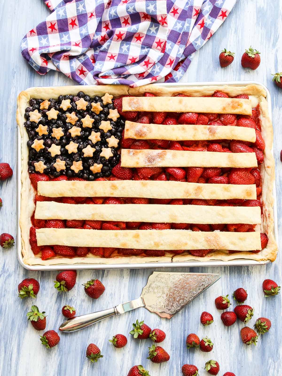 A rectangular pie, perfect for National Pie Day recipes, is decorated as an American flag with blueberries and star-shaped pastry in one corner and strawberries with pastry stripes. Fresh strawberries and a checkered cloth complete this best bloggers’ festive creation.