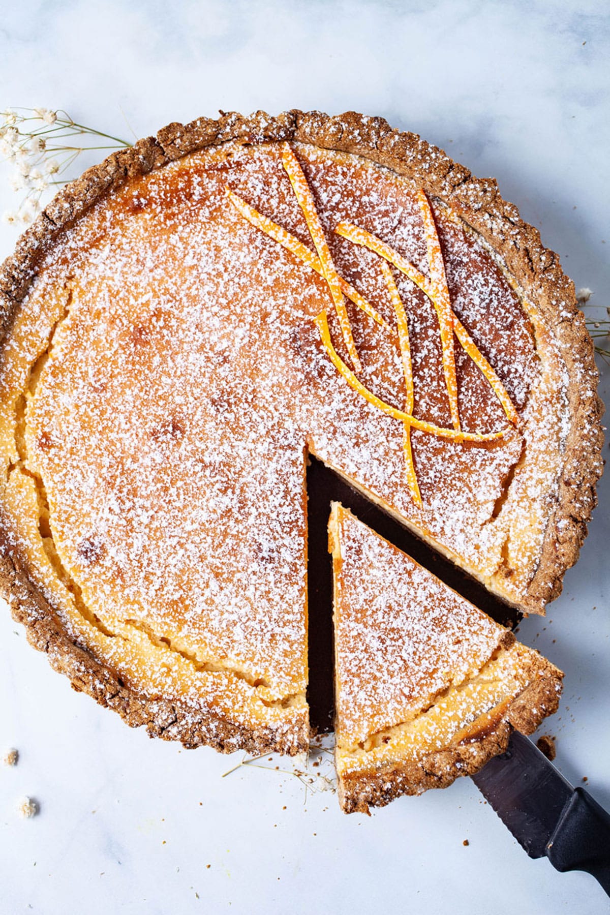 A round tart with a sugared crust, dusted with powdered sugar and orange peel strips on top, is featured as one of the National Pie Day Recipes celebrated by the best bloggers—one slice is being lifted out on a spatula.
