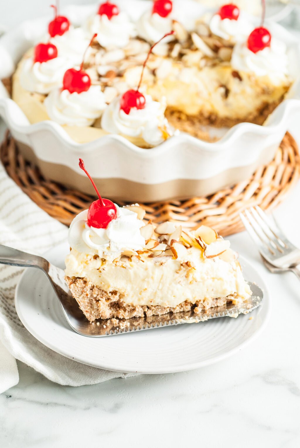 A slice of creamy pie topped with whipped cream, almond slices, and a cherry is served on a plate, perfect inspiration for National Pie Day recipes from the best bloggers. The rest of the pie sits temptingly in the background.