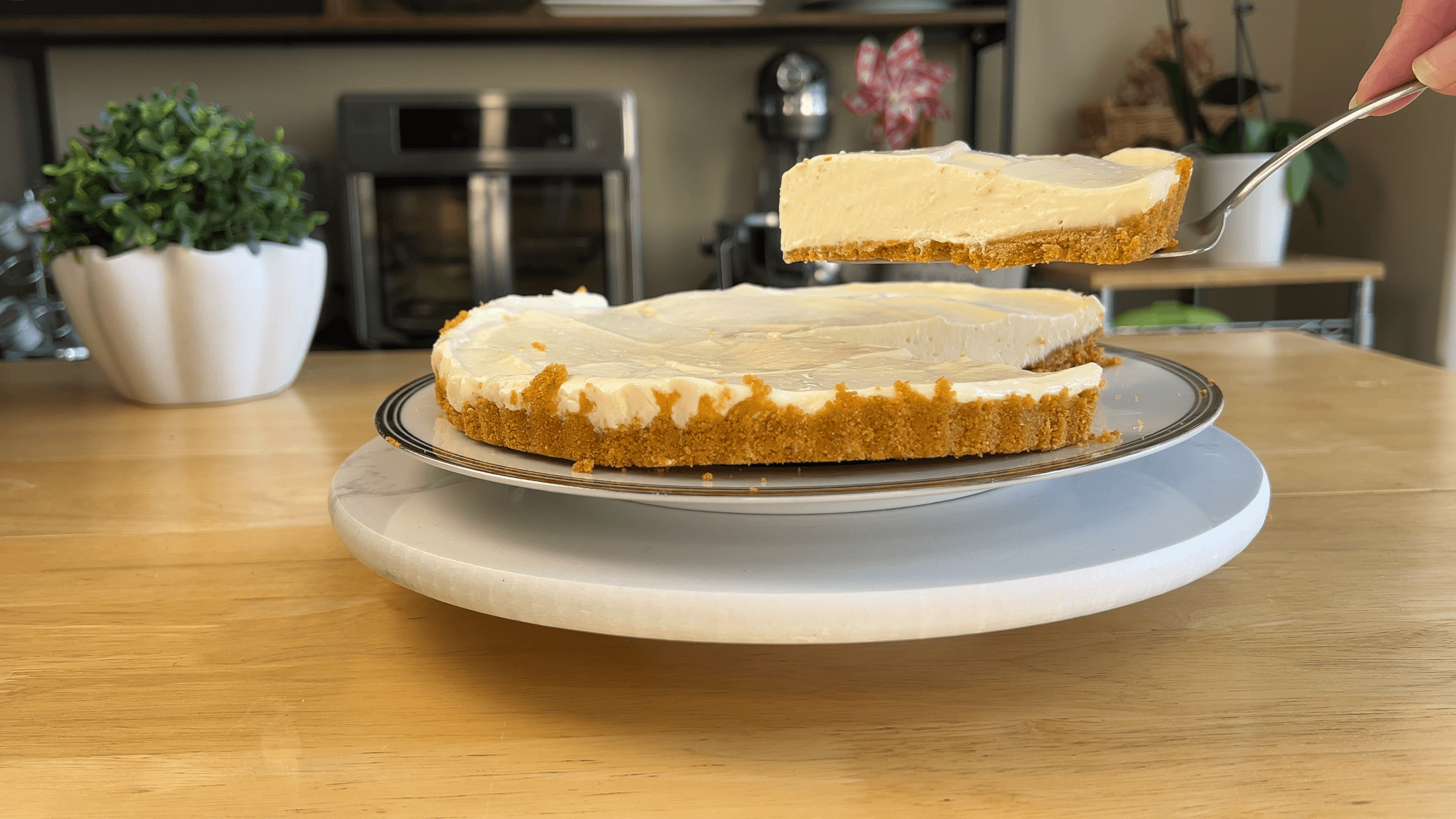 A cheesecake with a graham cracker crust on a plate, one slice being lifted by a spatula—perfect inspiration for an easy lemon tart recipe in your cozy kitchen setting.