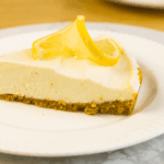 A slice of lemon cheesecake with a graham cracker crust, inspired by an easy lemon tart recipe, garnished with two lemon slices and served on a white plate.