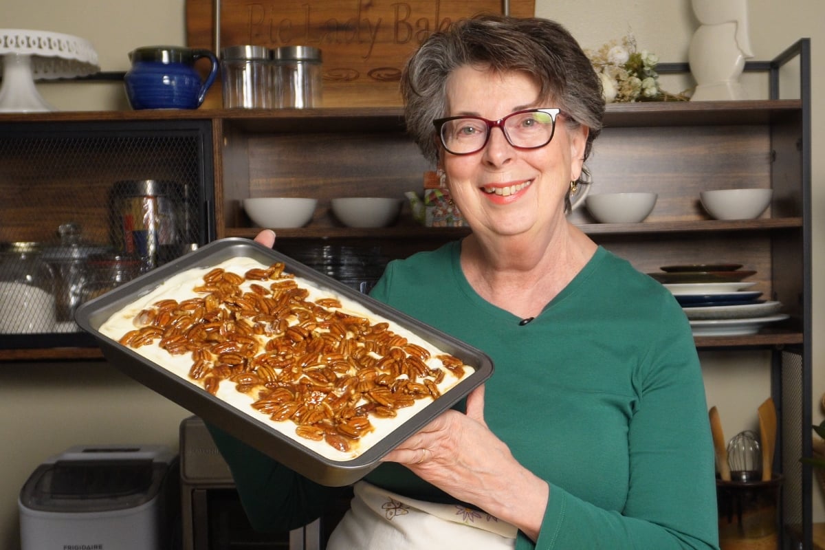 A smiling woman holds a rectangular baking pan filled with a pecan pie lasagna.