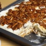 Rectangular pan of pecan pie lasagna with layered dessert fillings topped by a thick layer of glazed pecans.