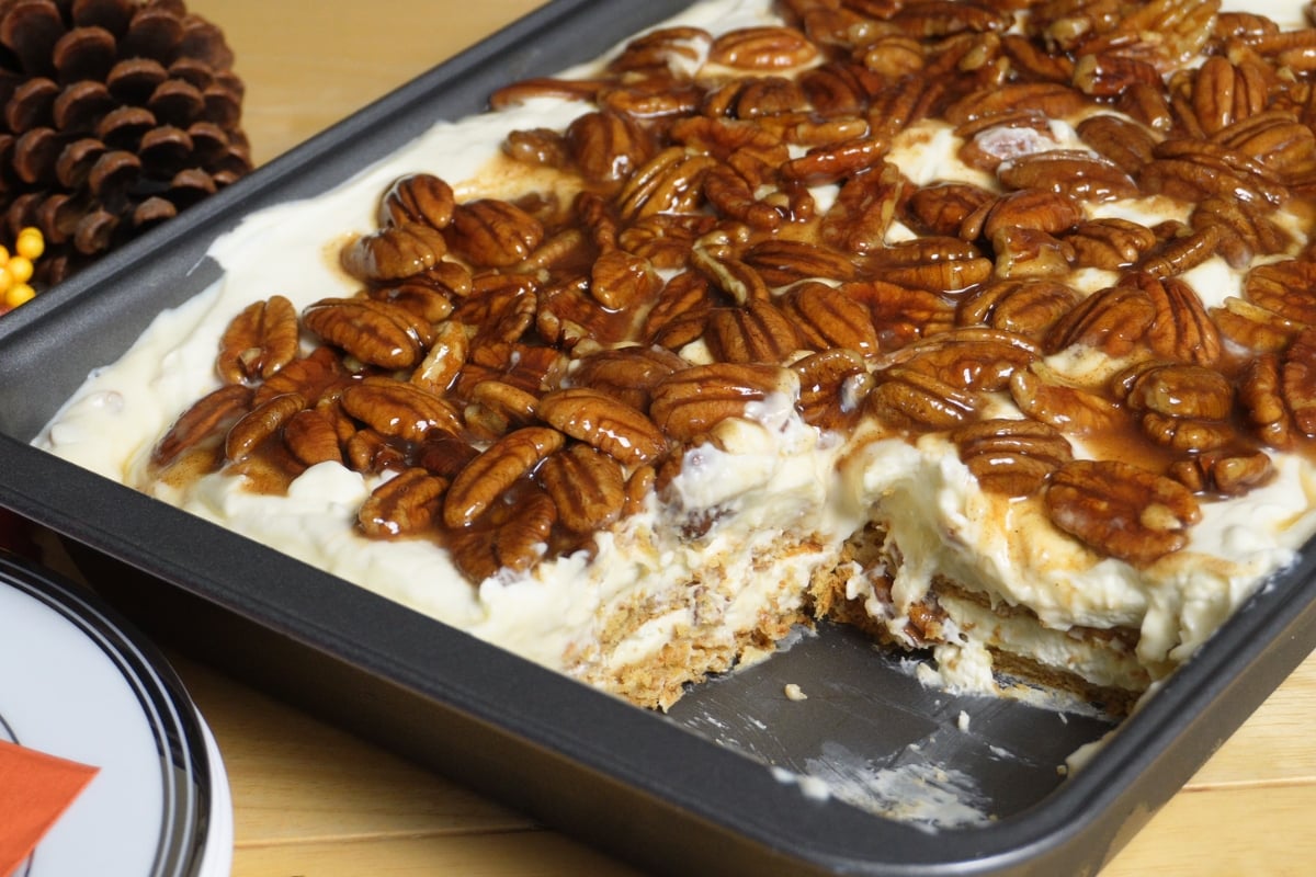 Rectangular pan of pecan pie lasagna with layered dessert fillings topped by a thick layer of glazed pecans.