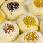 A plate of thumbprint cookies filled with various fruit jams and dusted with powdered sugar.