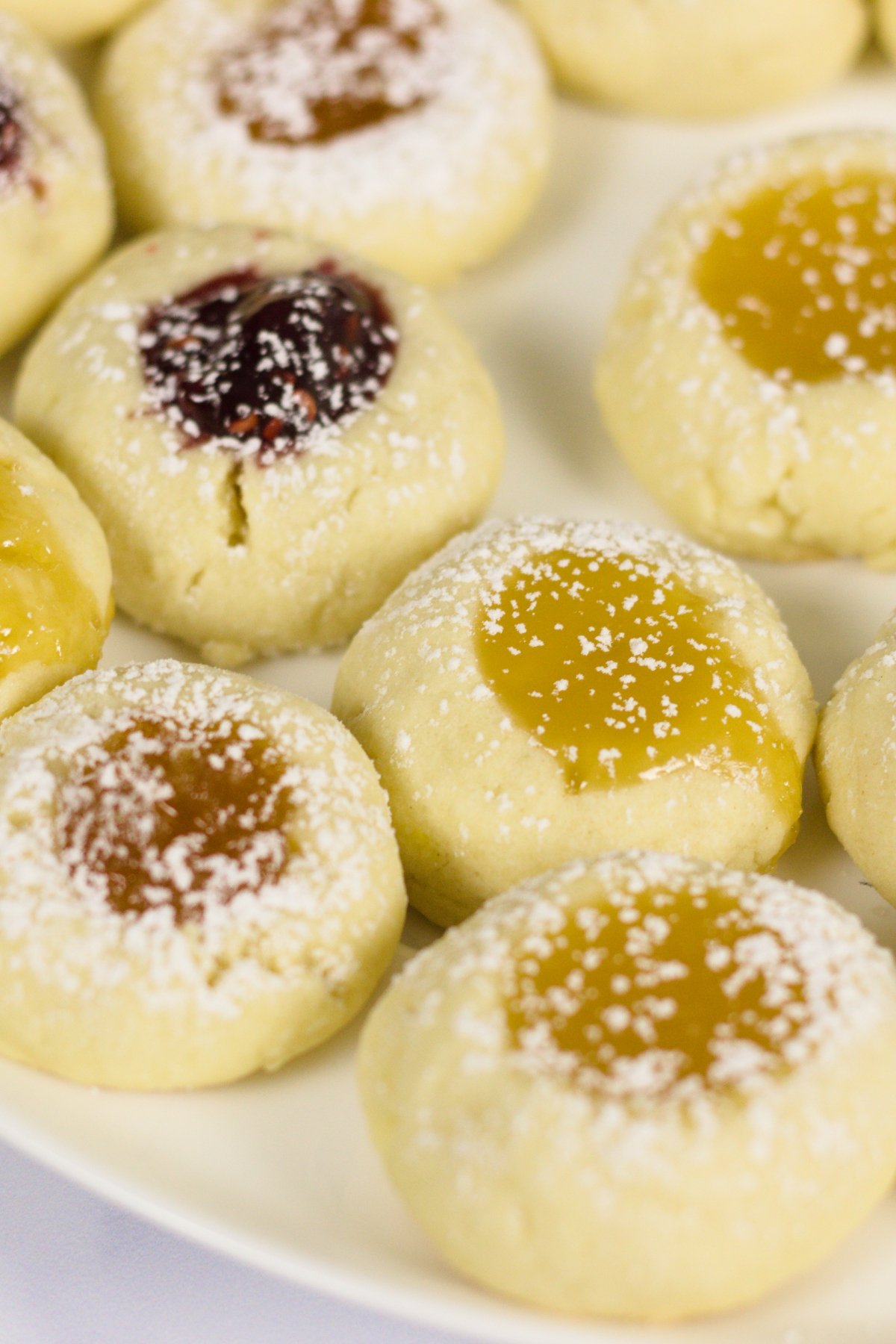 A plate of thumbprint cookies filled with various fruit jams and dusted with powdered sugar.