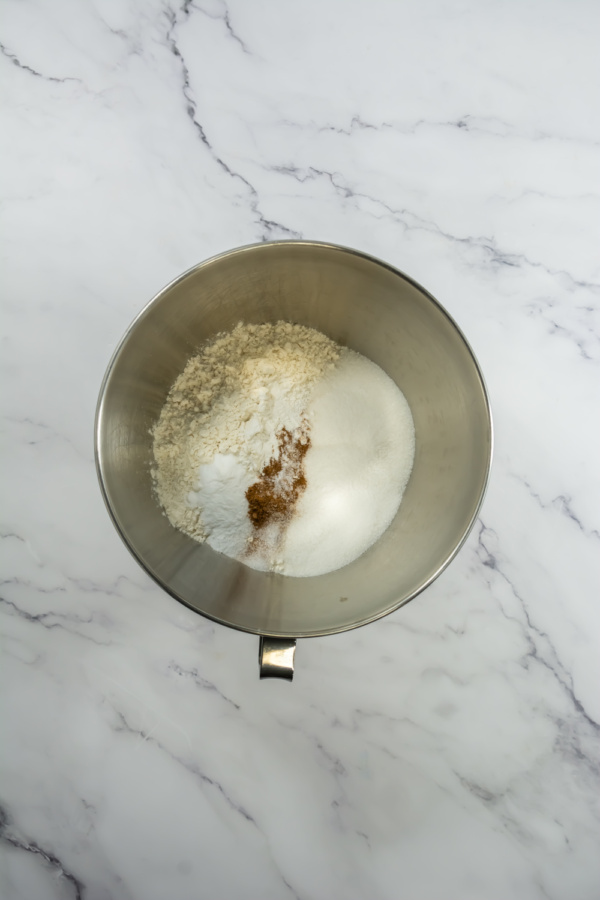 A metal mixing bowl containing flour, sugar, baking powder, and spices on a white marble countertop—perfect for recreating Starbucks Pumpkin Cream Cheese Muffins at home.