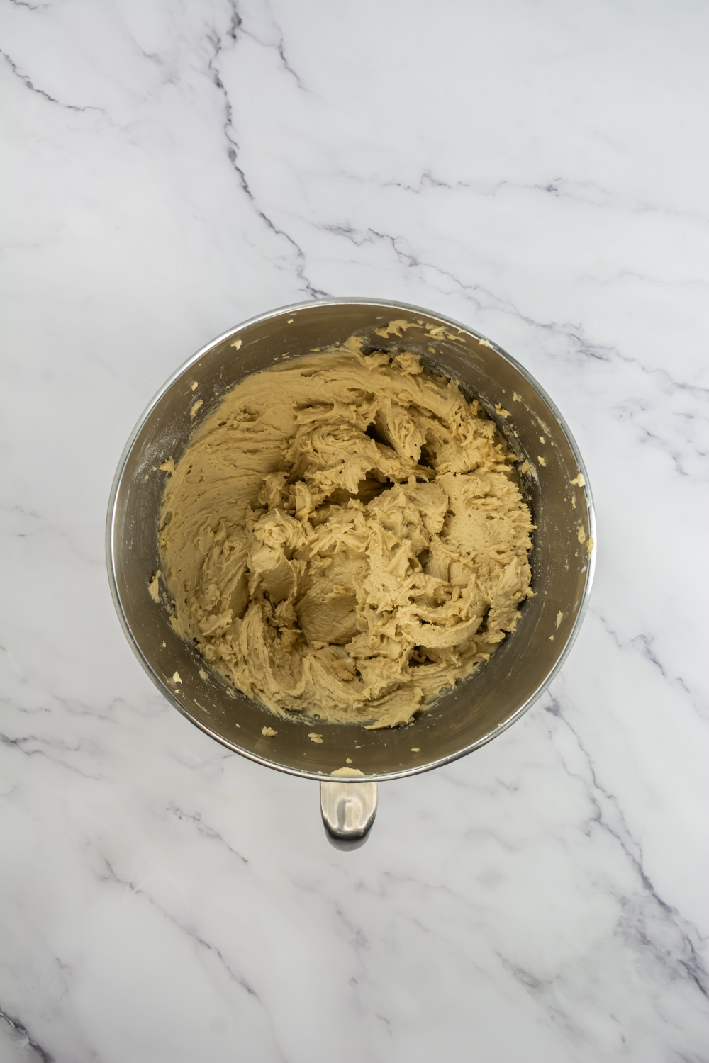 A metal mixing bowl filled with cookie dough sits on a white marble surface.