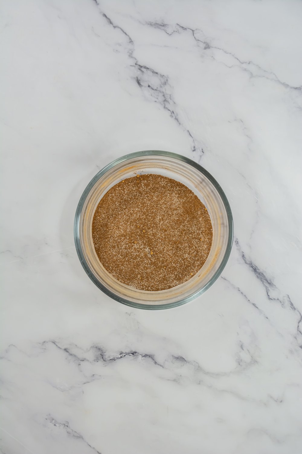 A glass bowl filled with a fine brown powder sits on a white marble surface.