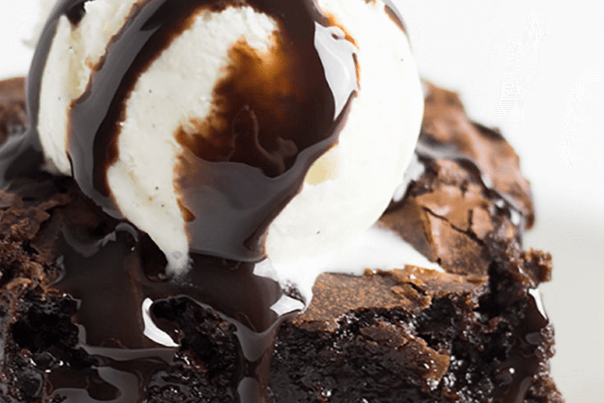A close-up of a chocolate brownie topped with a scoop of vanilla ice cream and drizzled with chocolate sauce.