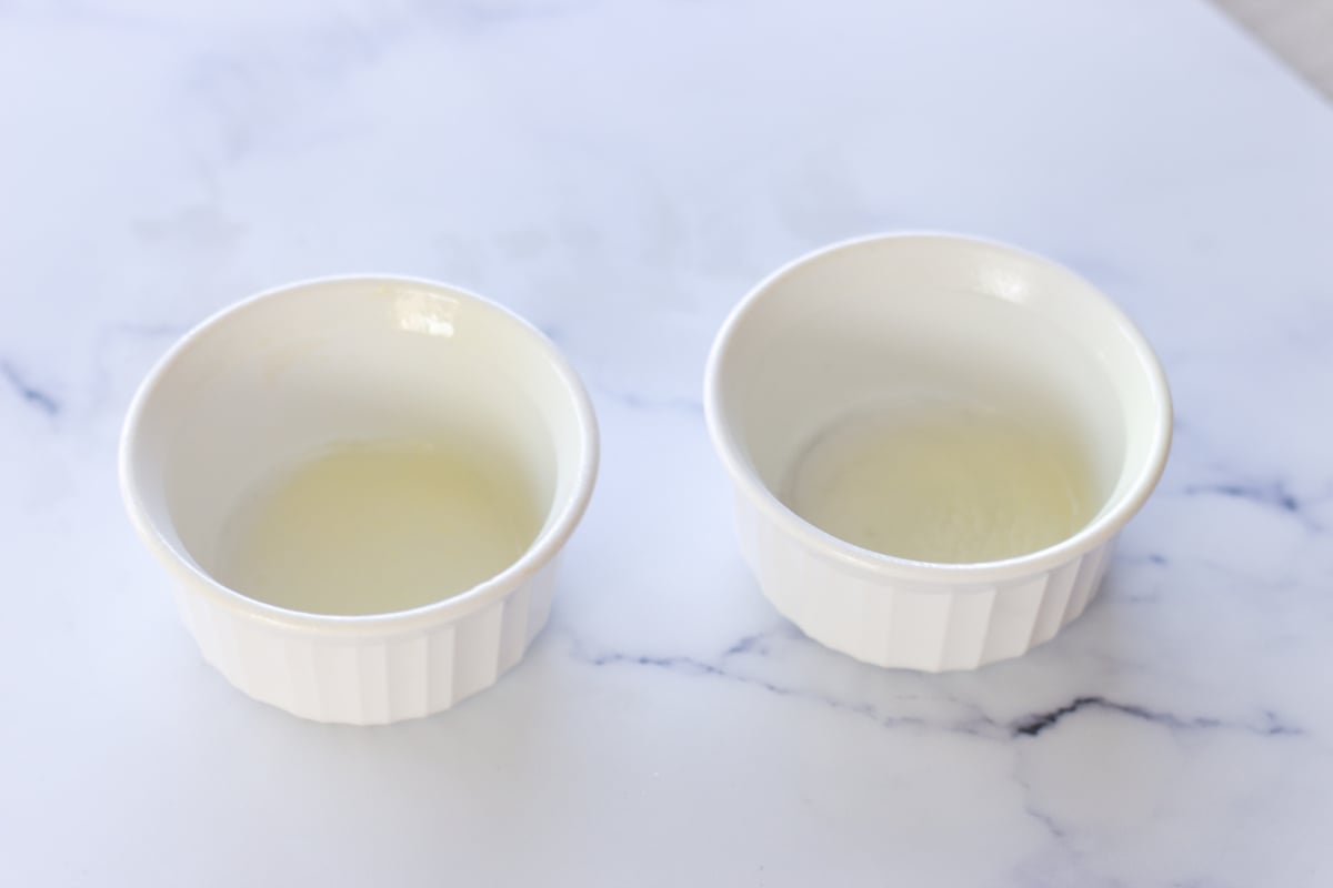 Two small white ramekins, each containing a small amount of egg white, on a white marble surface.
