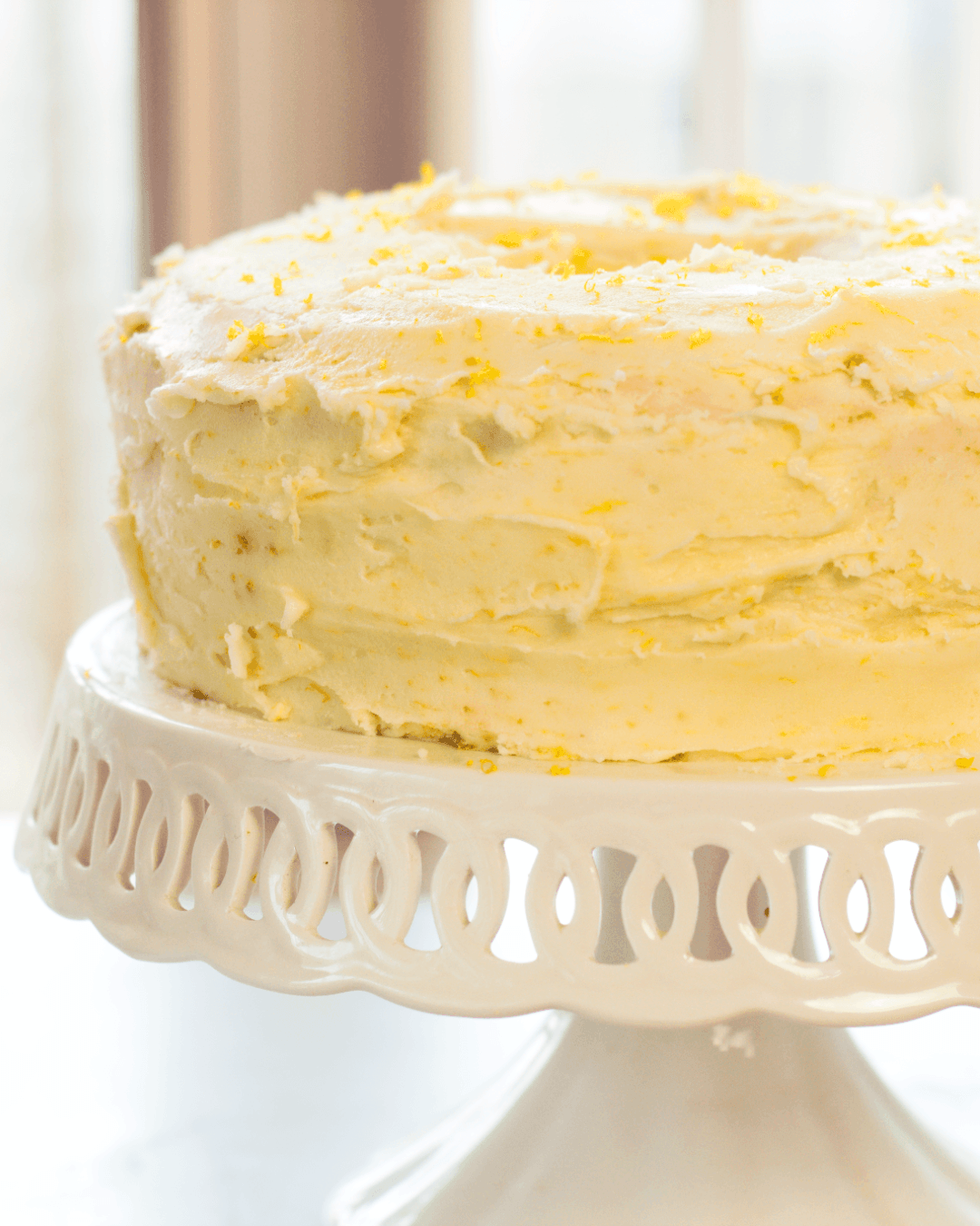 A frosted layer cake with a textured yellow and white icing sits on a white decorative cake stand.