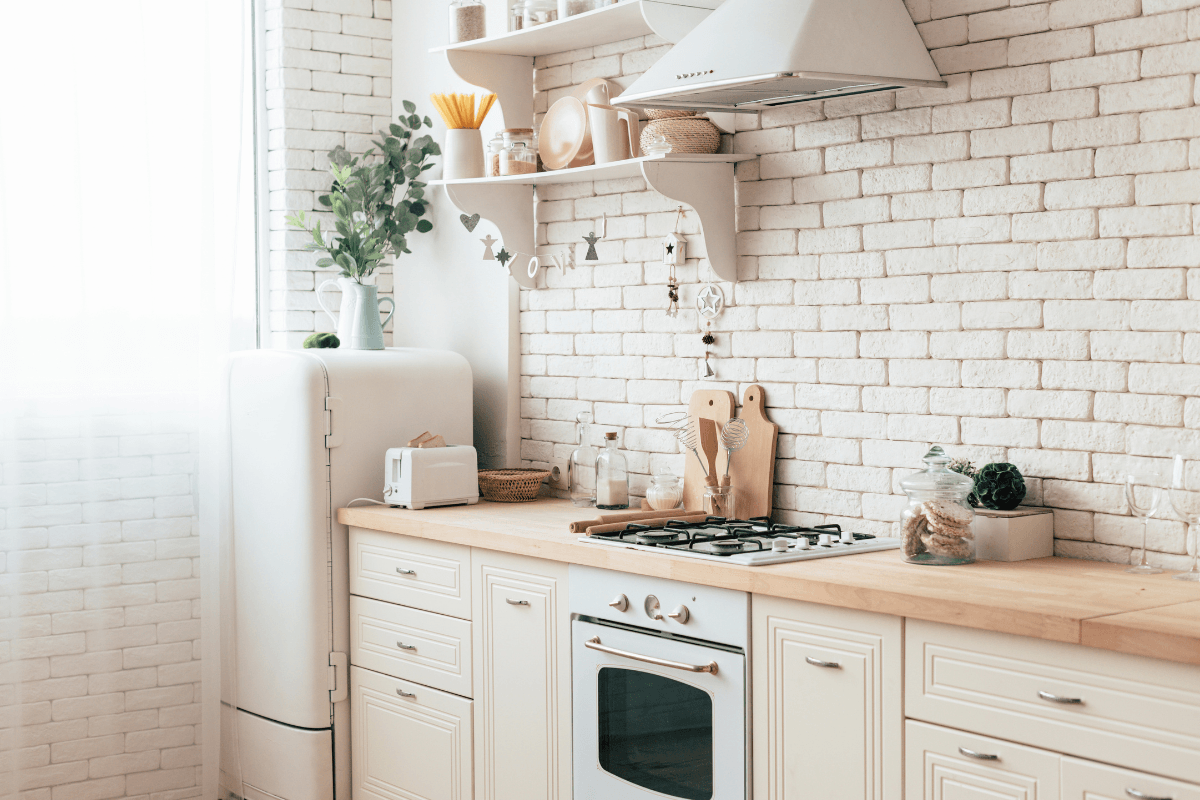 A bright kitchen with white brick walls, wooden countertops, white cabinets, a gas stove, oven, retro refrigerator, and open shelves with kitchen items and decor.