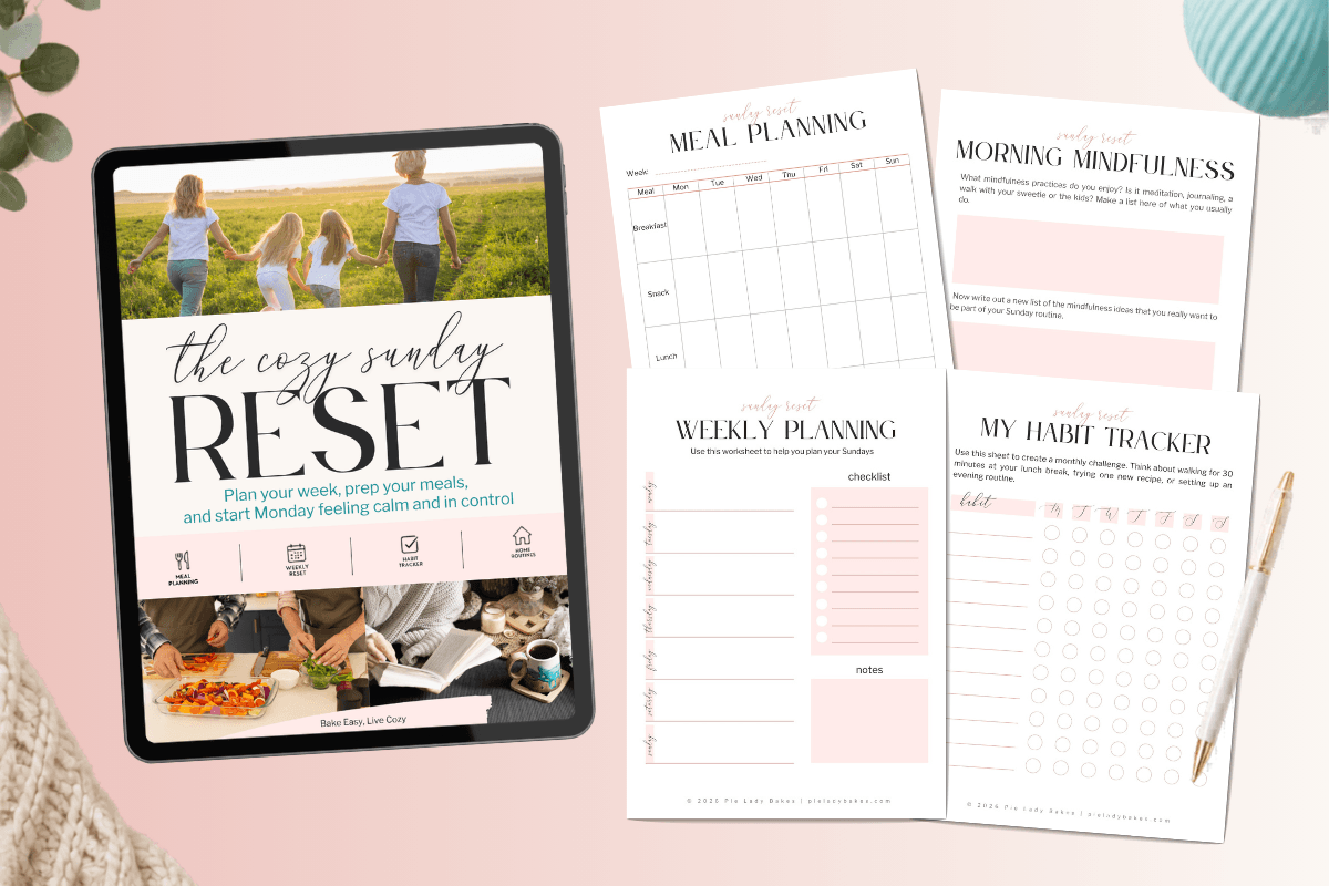 An iPad displays "The Cozy Sunday Reset" guide beside printable meal planning, morning mindfulness, weekly planning, and habit tracker sheets on a pink surface with a pen and a small plant.