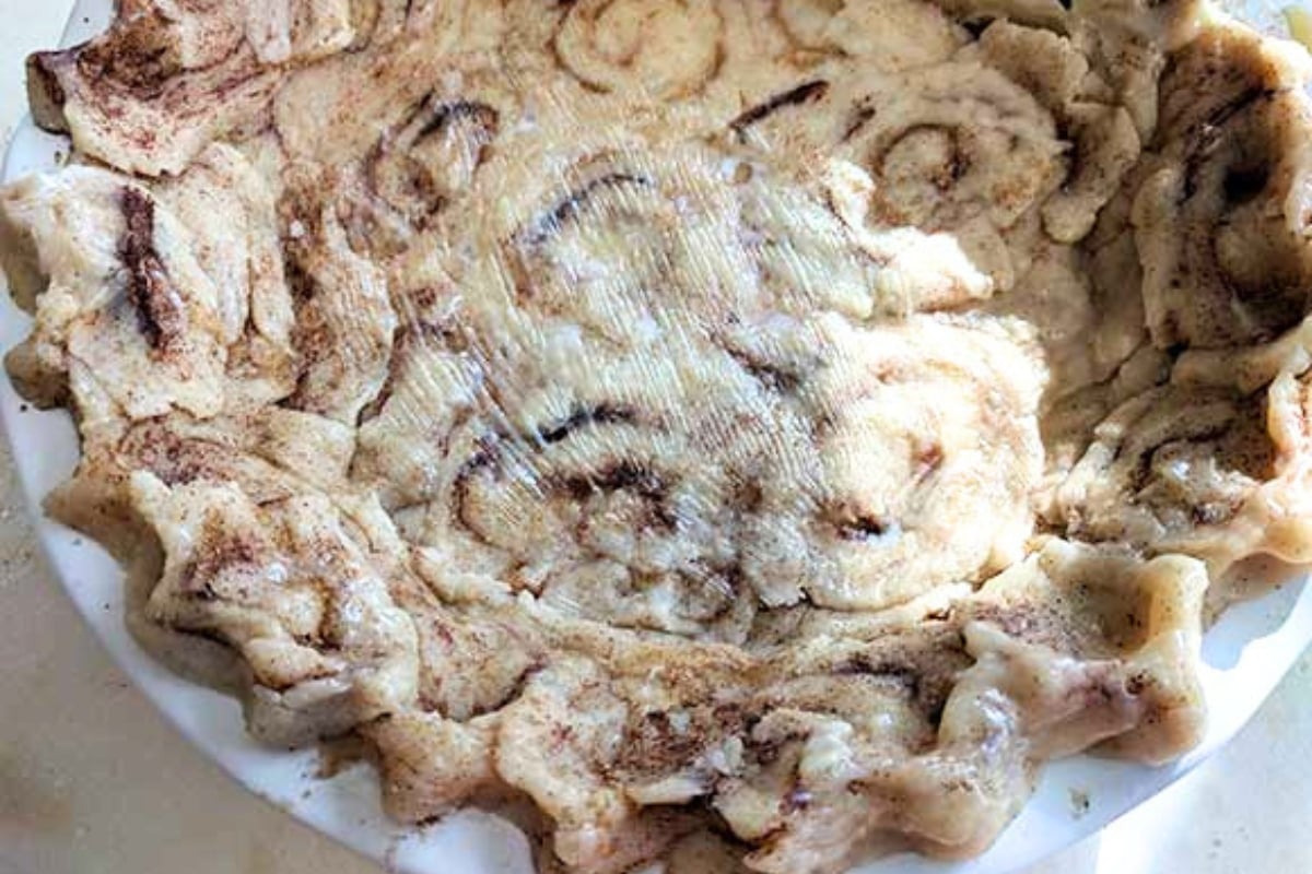 Unbaked cinnamon roll pie crust with visible swirls and crimped edges in a white pie dish, ready for filling—perfect for easy cinnamon roll desserts.
