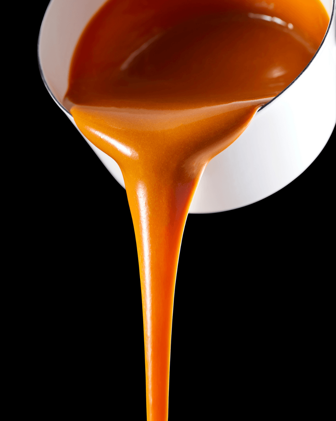 Caramel sauce being poured from a white container against a black background.