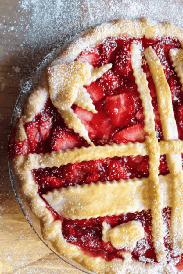 A freshly baked strawberry pie with a golden lattice crust and a dusting of powdered sugar on top.