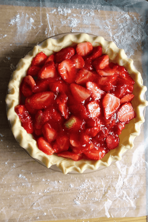 Unbaked strawberry pie with a crimped crust and fresh strawberry filling on a flour-dusted surface.