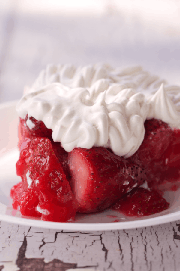 A slice of strawberry pie topped with whipped cream is served on a white plate, making it one of the easy strawberry desserts you'll love.