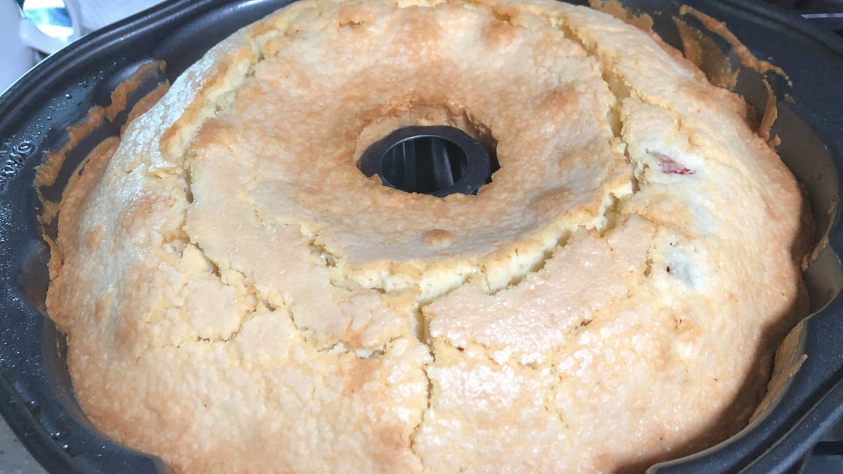 A golden brown bundt cake with a cracked top sits in a black bundt pan.