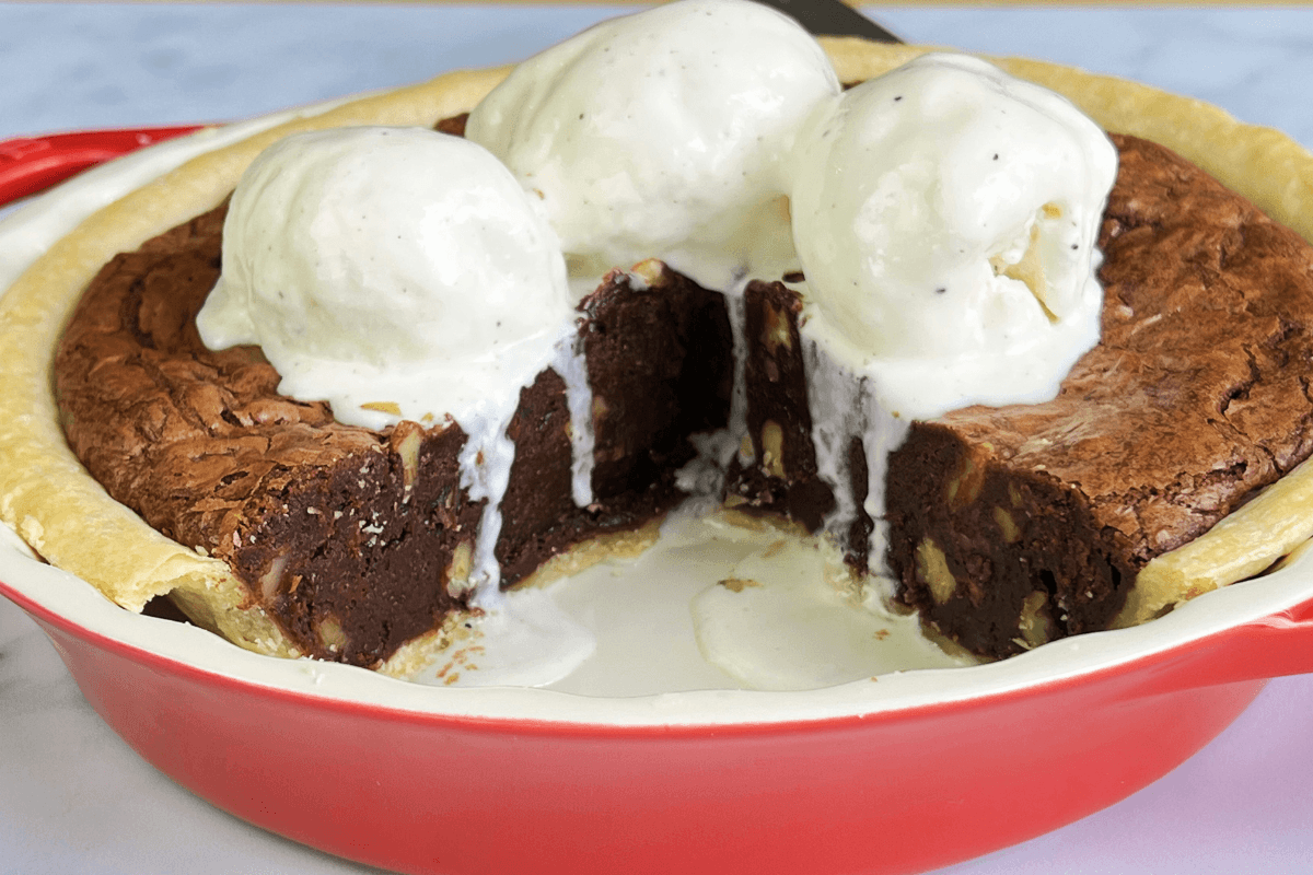 A chocolate brownie pie with a slice missing, topped with three scoops of vanilla ice cream, served in a red pie dish—one of the easiest desserts with store bought pie crust you'll ever try.