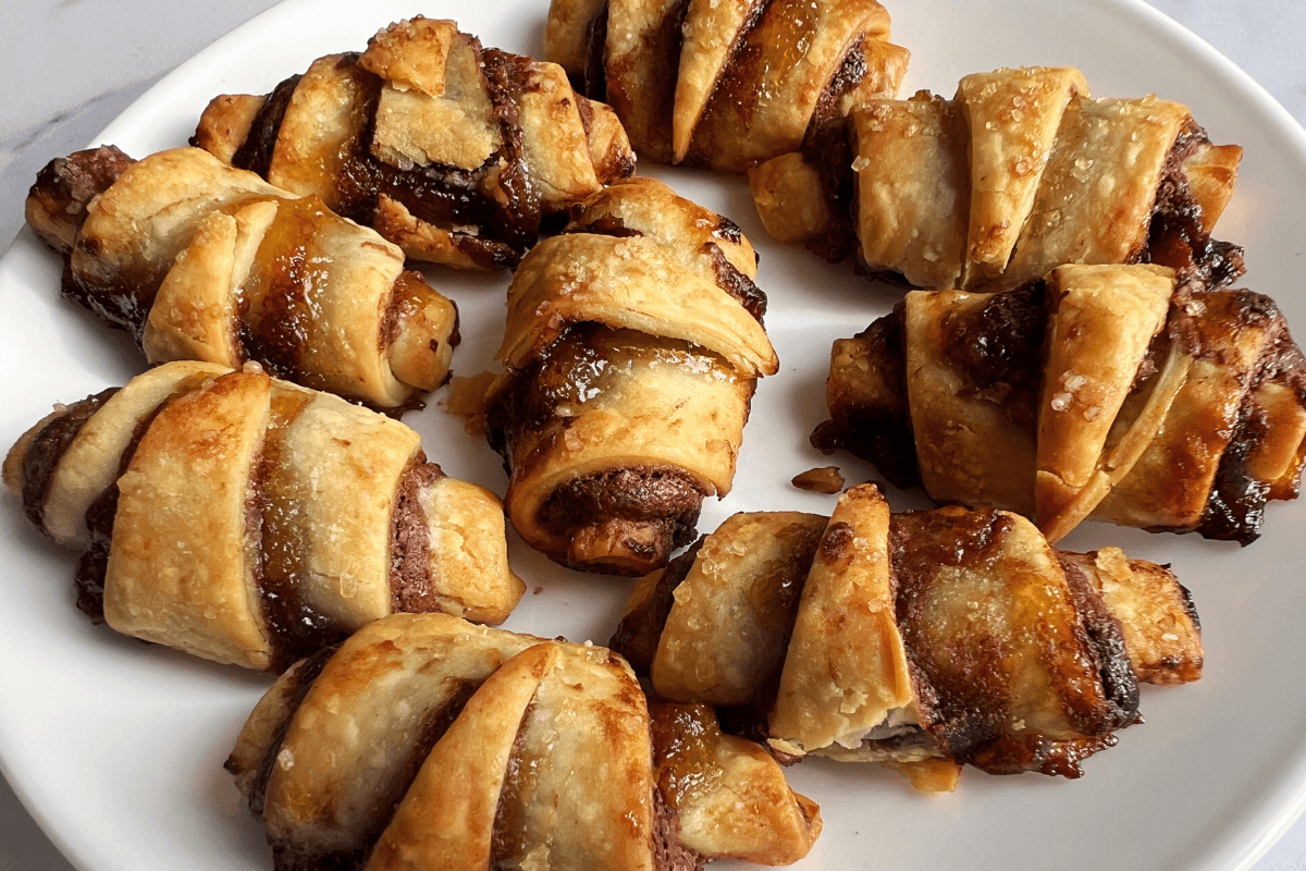 A white plate with eight baked rugelach pastries filled with cinnamon and chocolate, topped with coarse sugar—an easy dessert with store bought pie crust perfect for anyone wondering what to make with pie crust.